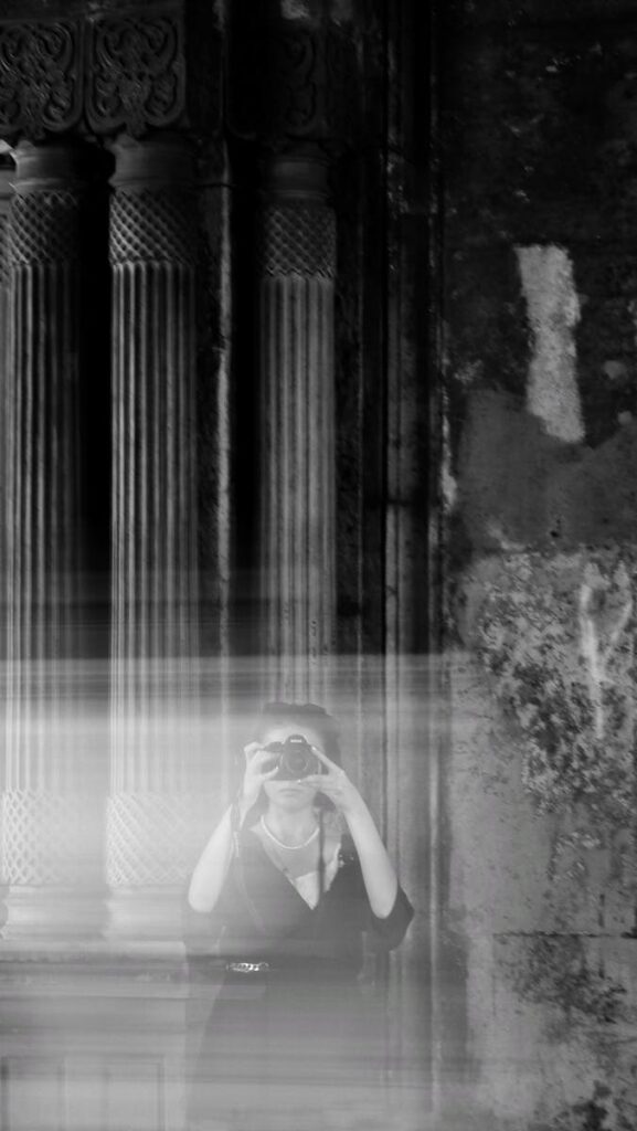 A mysterious black and white reflection of a photographer with blurred effects in an ancient setting.